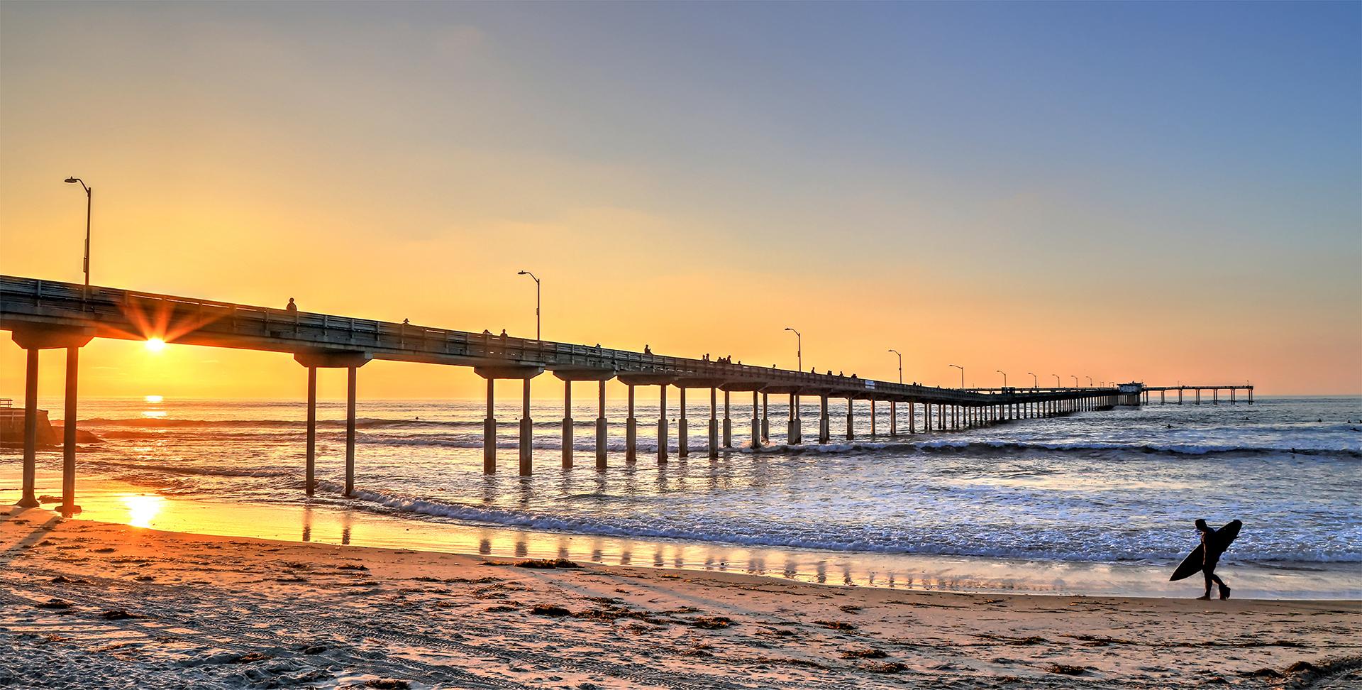 San Diego pier at the beach with a man walking and holding a surfboard
